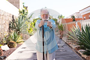 Front view of attractive smiling senior man in outdoors looking at camera holding a walking cane