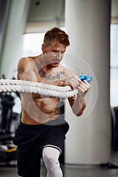 Front view of Attractive young fit and toned sportswoman working out with battle ropes. Motion blur