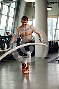 Front view of Attractive young fit and toned sportswoman working out with battle ropes. Motion blur