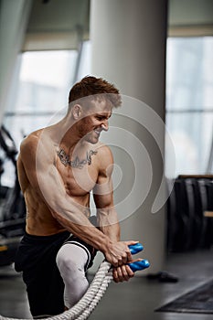 Front view of Attractive young fit and toned sportswoman working out with battle ropes. Motion blur