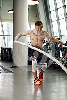 Front view of Attractive young fit and toned sportswoman working out with battle ropes. Motion blur