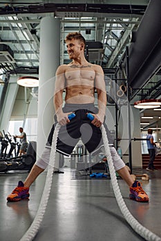 Front view of Attractive young fit and toned sportswoman working out with battle ropes. Motion blur