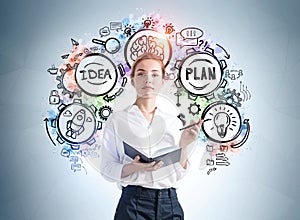 Front view of attractive young woman in formal wear holding a planner and standing near grey wall with creative colorful idea