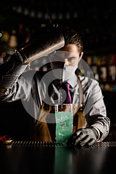 front view of bartender pouring blue cocktail from steel shaker into cup