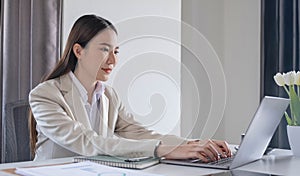 Front view of a beautiful Asian businesswoman working on a tablet coffee cup placed on the office table.