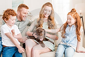 Front view of beautiful redhead family playing with puppy at home