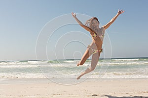 Front view of beautiful young Caucasian woman in bikini jumping on the beach