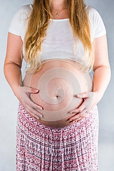 Front view on belly with stretchmarks of pregnant woman on light background photo