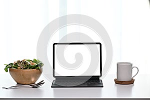 Front view of blank screen computer tablet with coffee cup and bowl of salad on table.