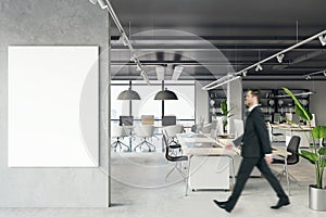 Front view of blank white isolated poster on a light grey wall at the entrance to modern loft office interior with concrete floor