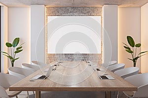Front view on blank white poster on brick wall in stylish board room with wooden meeting table with modern laptops surrounded by