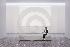 Front view on blank white poster with place for your logo on light wall background in spacious gallery hall with businesswoman