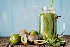 Front view of blended green smoothie with kiwi, lime and mint isolated on blue wooden background