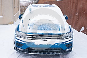 Front view blue modern car covered in snow is parked in the yard