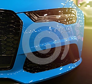 Front view of blue modern luxury sport with soft orange sun light. Car exterior details. Headlight of a modern sport car.