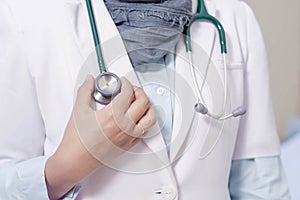 Front view body part of hijab female doctor hand holding stethoscope head inside a hospital bed room using white lab coat uniform