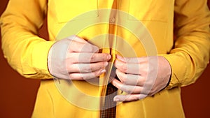 Front view on body part of young female in yellow blouse. Close up of unrecognizable woman unbutton her blouse on orange