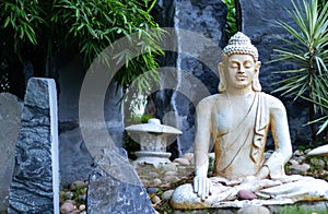 Front view of a Buddha statue with blue grey rocks in the background and bamboo trees. Enlightment concept