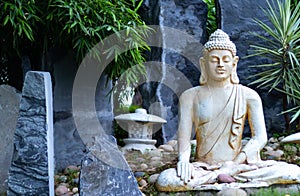 Front view of a Buddha statue with blue grey rocks in the background and bamboo trees. Enlightment concept photo