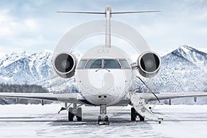 Front view of the business jet with an opened gangway door at the winter airport apron on the background of high scenic mountains