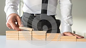 Front view of a businessman arranging wooden pegs in to a staircase shape