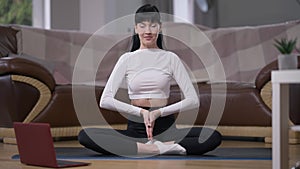 Front view calm confident female yogi sitting in lotus pose meditating inhaling and exhaling in slow motion. Wide shot