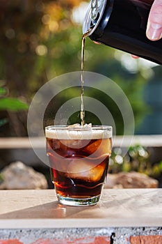 Front view of a can pouring soft drink over a glass with ice on a wallflower outdoors on a summer evening. photo