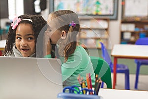 Front view of Caucasian schoolgirl whispering a secret into friend ear while her friend seem astonis