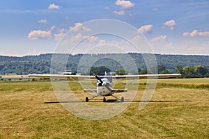 Front view of Cessna 172 airplane standing on grass field with blue cloudy sky on the background.