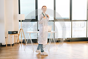 Front view of charming female doctor in white coat standing on background of window in sunny day in light medical clinic