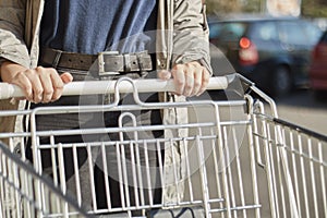 Front view closeup with a selective focus of a teenage girl moving a shopping cart outside a supermarket