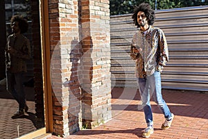 Front view of a cool young smiling afro man using a mobile phone while standing outdoors in a sunny day