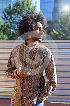 Front view of a cool young smiling afro man using a mobile phone while standing outdoors in a sunny day