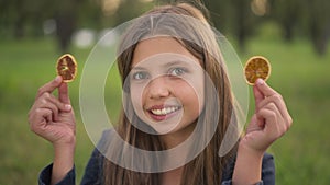 Front view cute cheerful teenage girl grimacing covering eyes with dried lemon smiling looking at camera. Portrait of