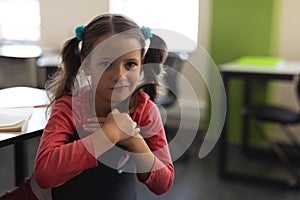 Front view of cute schoolgirl looking at camera and sitting at desk in classroom