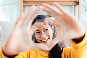 Front view of cute young Asian woman smiling and looking at camera with hands showing heart shape