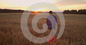 Front view : An elderly male farmer walks through a wheat field at sunset. The camera follows the farmer walking on the
