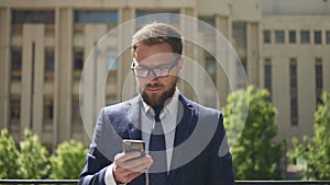 Front view of elegant businessman is using smartphone standing on city building background.