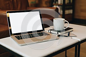 Front view. Empty workplace. On white coffee table is laptop with blank screen, cup of coffee, notebook, pen, newspaper.