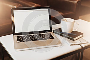Front view. Empty workplace. On white coffee table is laptop with blank screen, cup of coffee, notebook, pen, newspaper.