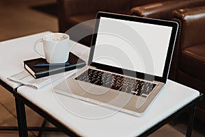 Front view. Empty workplace. On white coffee table is laptop with blank screen, cup of coffee, notebook, pen, newspaper.