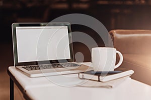 Front view. Empty workplace. On white coffee table is laptop with blank screen, cup of coffee, notebook, pen, newspaper.