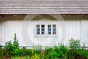 Front view of the facade of the old house. White painted boards and a shingled roof. Beautiful little garden