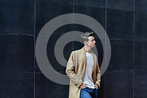 Front view of a fashionable young man standing against black wall while looking away outdoors in the street