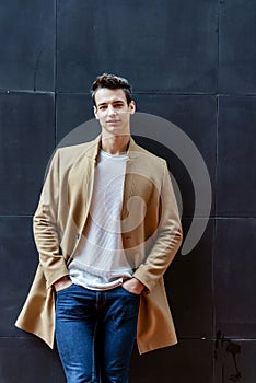 Front view of a fashionable young man standing against black wall while looking camera outdoors in the street