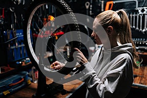 Front view of focused blonde female cycling repairman checking bicycle wheel spoke with bike spoke key in repair