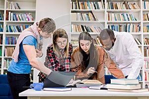 Front view of four concentrated multiethnic young people, college students preparing to their homework in library room