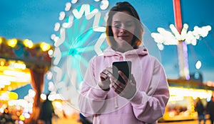 Front view girl pointing finger on screen smartphone on defocus background bokeh light in evening street attraction, woman using