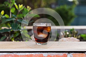 Front view of a glass filled with cola and ice, on a wallflower on an outdoor terrace on a summer evening. photo