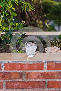 Front view of a glass full of ice and water on a brick wallflower on a terrace. Outside, summer evening. photo